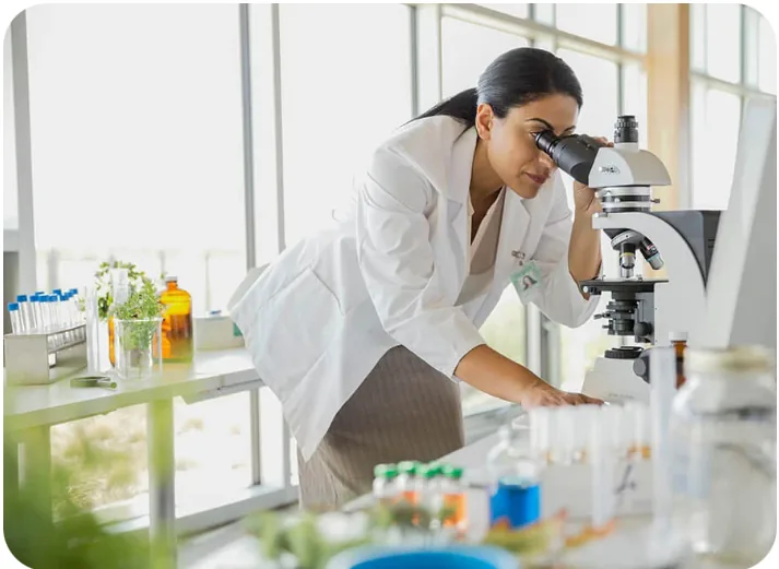 Scientist in a white lab coat examining a sample through a microscope in a life sciences laboratory