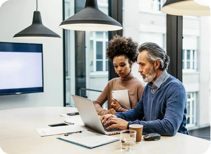 Two finance colleagues reviewing figures on a laptop screen together in a meeting room