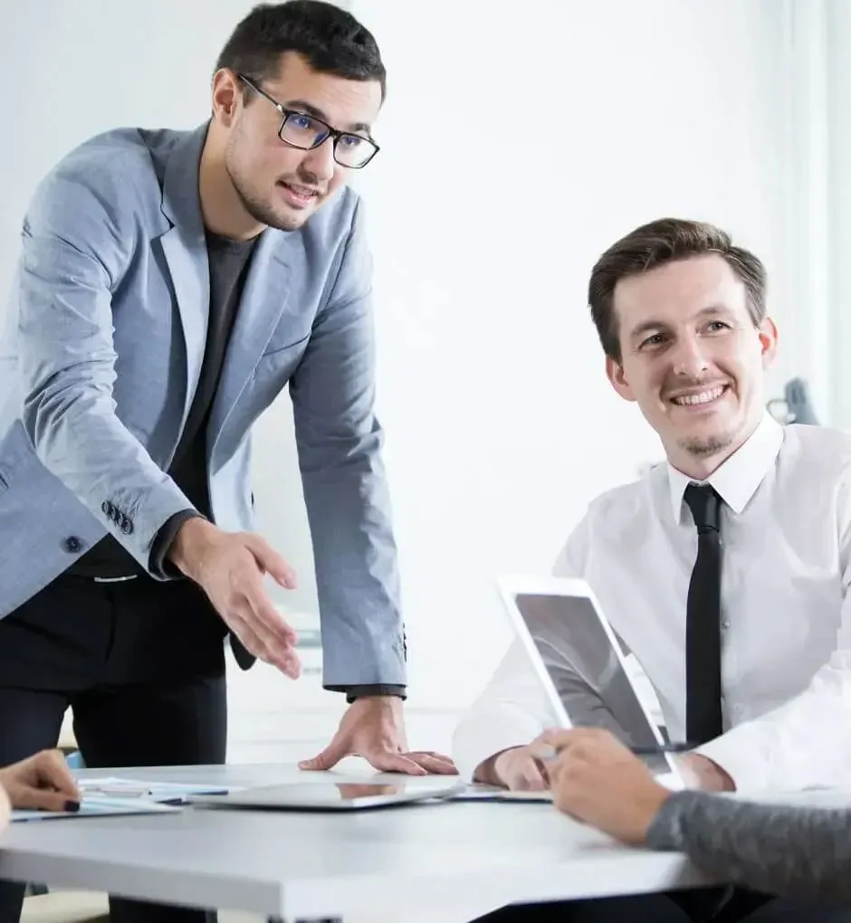 Two advisers reviewing documents and a tablet across a meeting table in a bright office