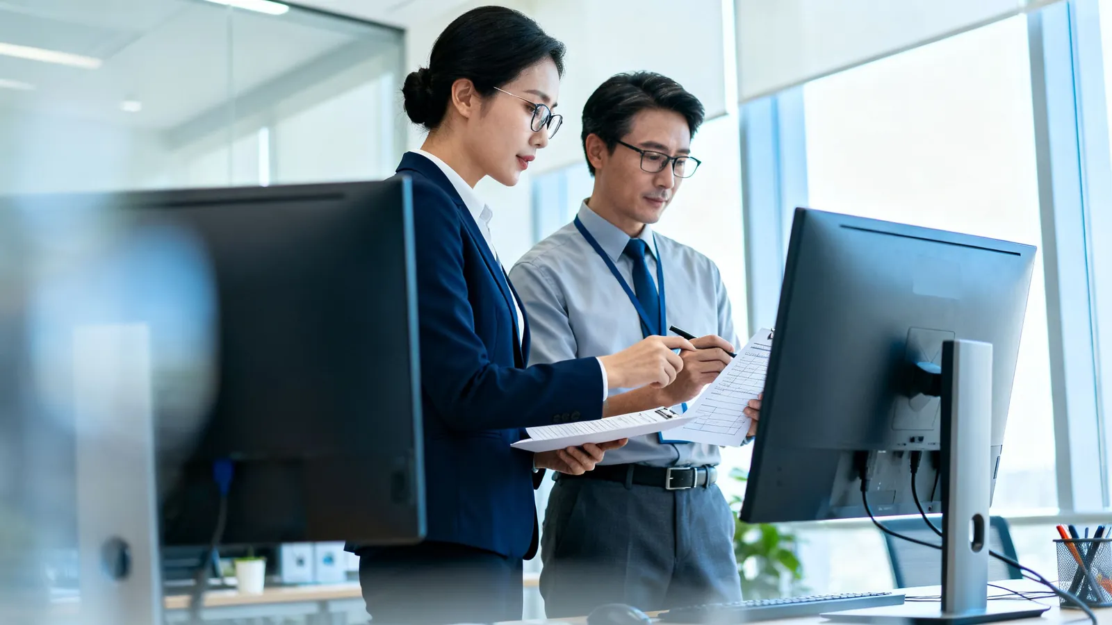 An analyst and an accountant comparing records on two monitors
